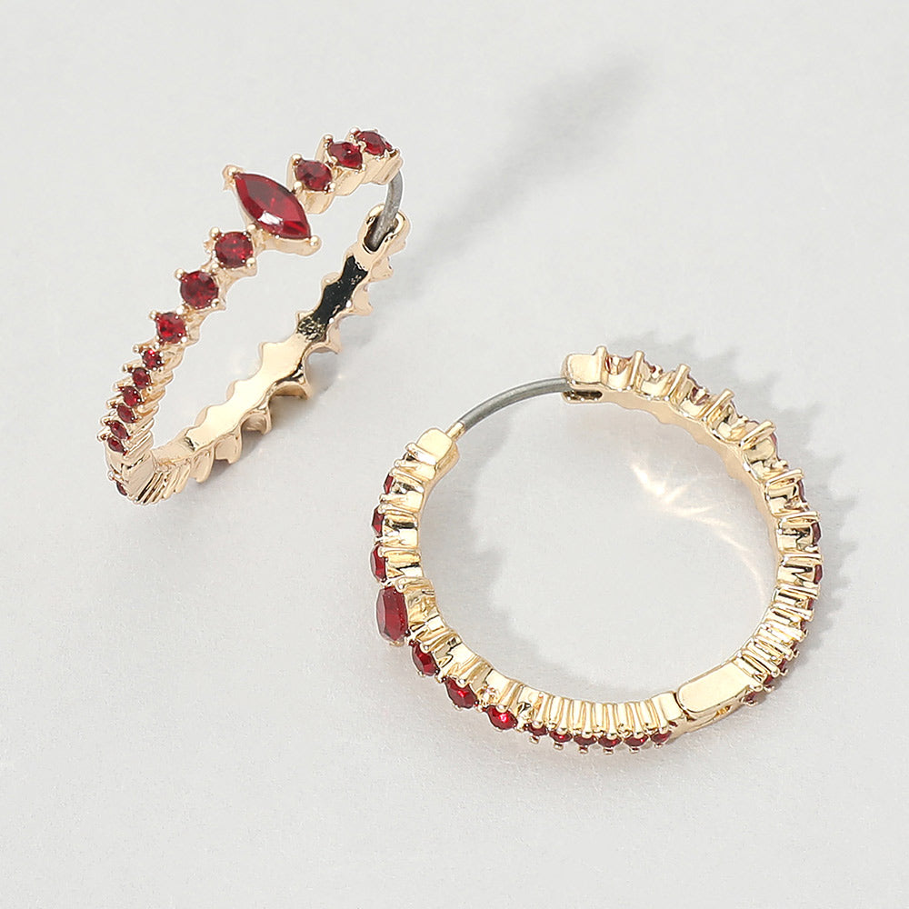 A pair of gold huggie hoop earrings with red marquise and round gemstones, displayed on a light gray background. 
