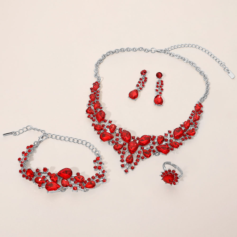 Red crystal 4-piece jewelry set on silver with statement necklace, matching bracelet, drop earrings and adjustable ring arranged on a light beige background.