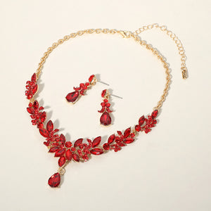 Red crystal teardrop and marquise leaf necklace set on gold with matching earrings, bold statement jewelry for bridal, prom, and evening wear on a beige background