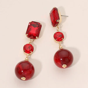Red faceted crystal and ball drop statement earrings on gold with rectangular, round, and spherical red stones, displayed on a light beige background.