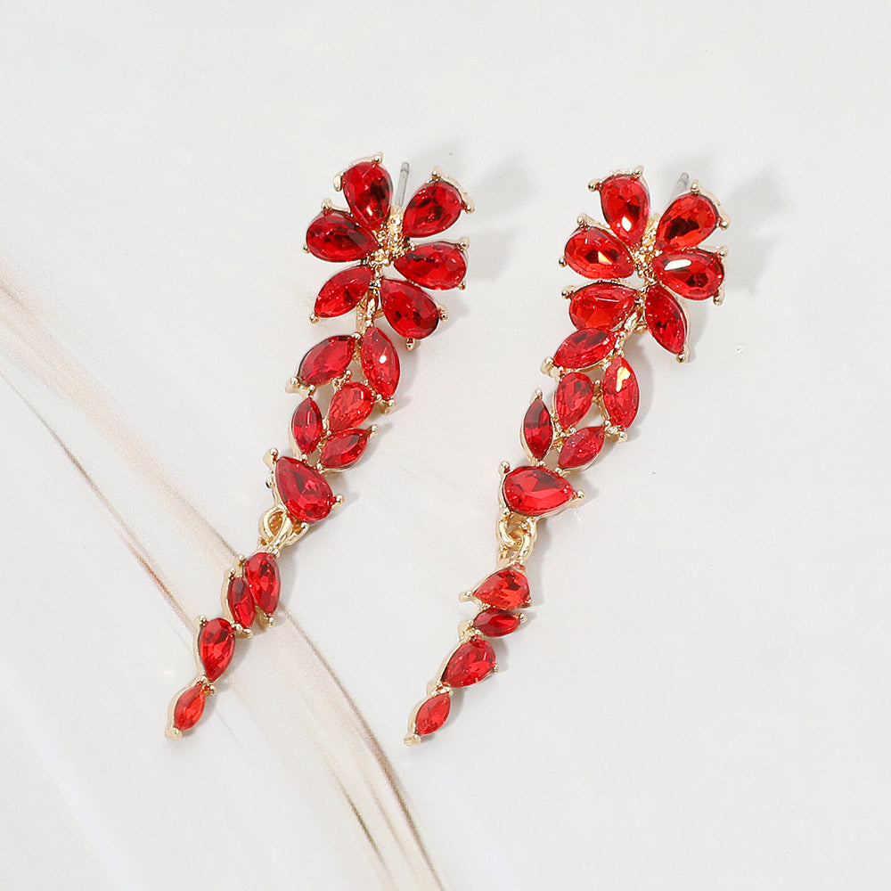 Gold-tone drop earrings featuring red marquise and round faceted crystals arranged in an elongated floral vine design, displayed on a white background .