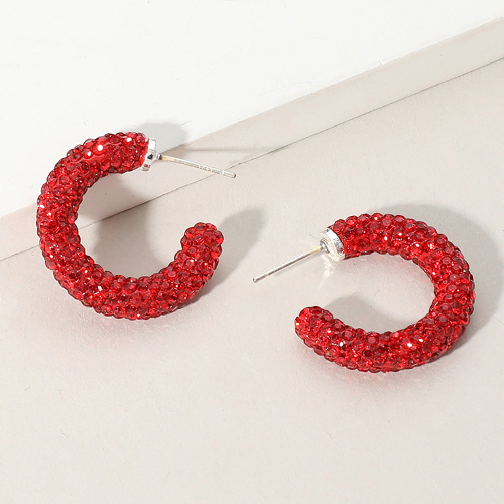 Red pavé half hoop earrings in a silver finish featuring rows of small red crystals covering the front of each hoop, displayed on a light beige background.