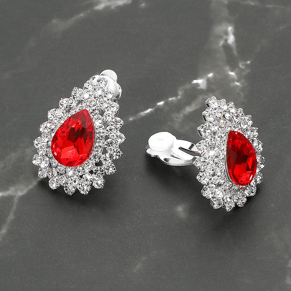 Small red teardrop crystal cluster clip-on earrings with layered rhinestone halo — elegant non-pierced jewelry for bridal, prom, and evening events on a dark marble background. 
