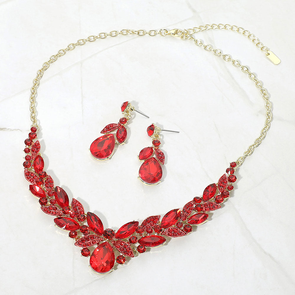 Red teardrop and marquise crystal jewelry set on gold displayed on white marble background