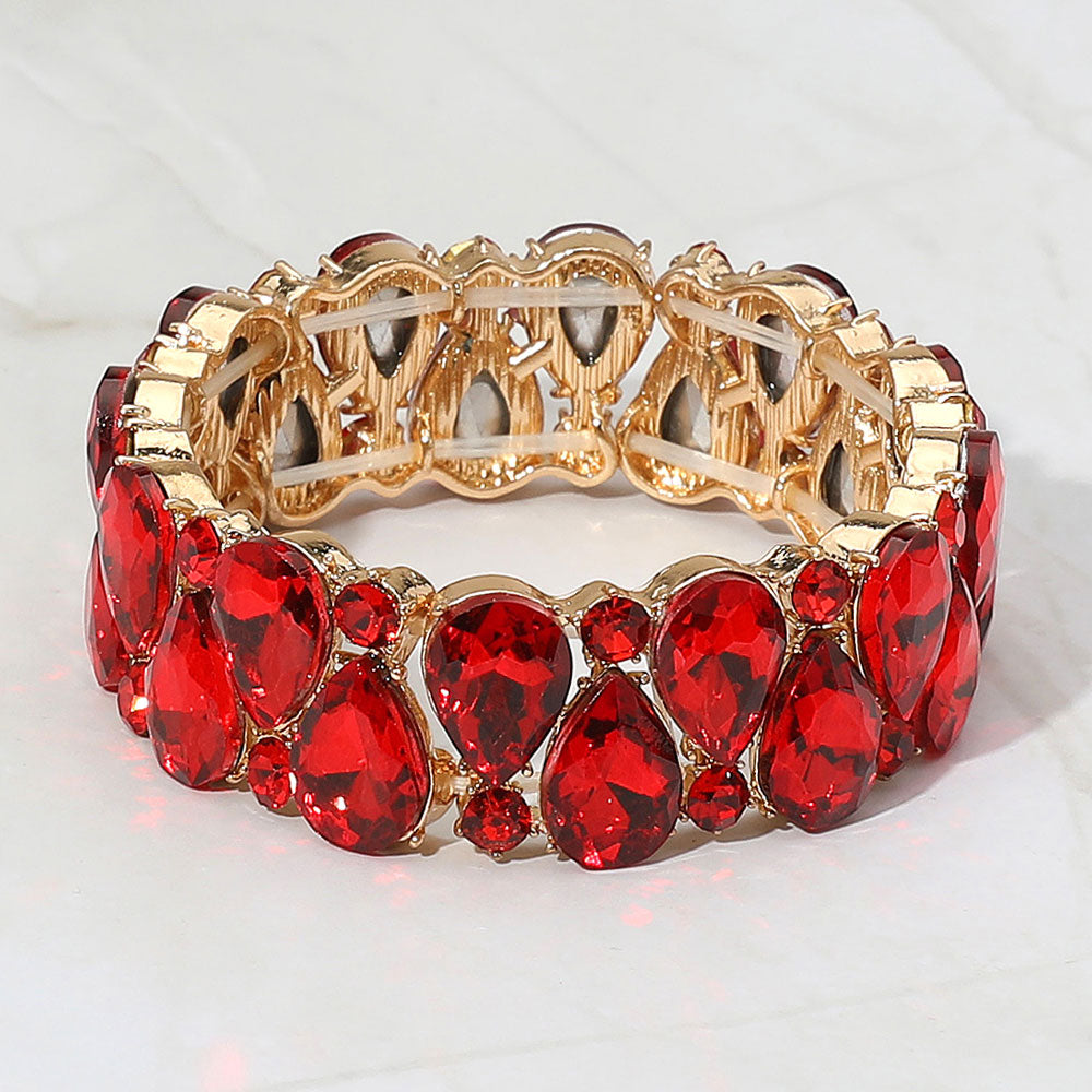Red teardrop and round stone cluster stretch bracelet on gold on white marble background