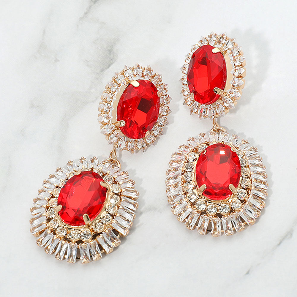 Red vintage double oval crystal statement earrings in a gold finish featuring two oval red crystals surrounded by clear crystal halos, displayed on a white marble background.
