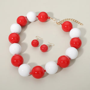 Red and white chunky ball beaded statement necklace set with oversized round beads and matching earrings, displayed on a beige background.