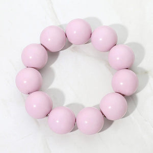 Pink chunky ball beaded stretch bracelet with oversized round beads, displayed on a white marble background.