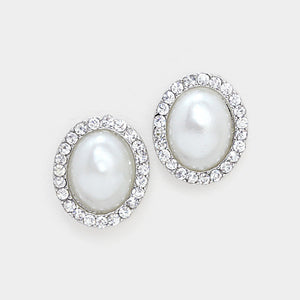 Close-up of white faux pearl oval stud earrings surrounded by clear rhinestones on silver-tone metal against a white background.