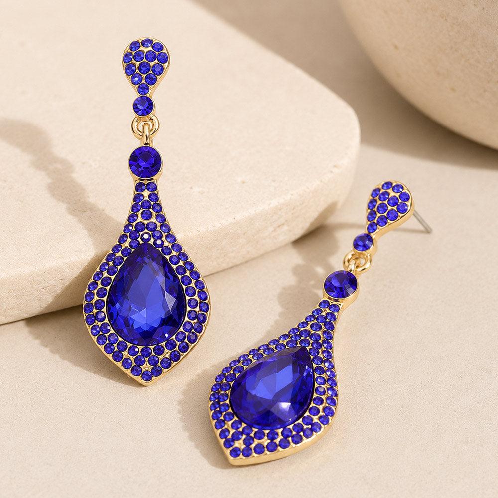 Sapphire royal blue crystal teardrop drop earrings on gold featuring a large blue teardrop crystal surrounded by smaller blue crystals, displayed on a neutral beige background.