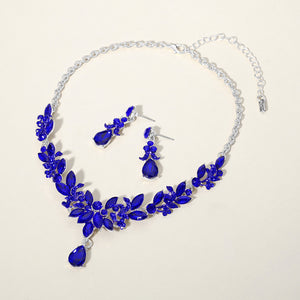 Sapphire royal blue crystal teardrop and marquise leaf necklace set on silver with matching earrings, elegant statement jewelry for prom and evening wear on a beige background