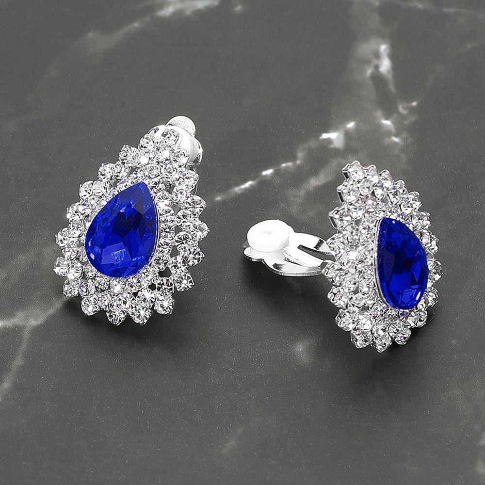 Small sapphire teardrop crystal cluster clip-on earrings with layered rhinestone halo — elegant non-pierced jewelry for bridal, prom, and evening events on a dark marble background. 