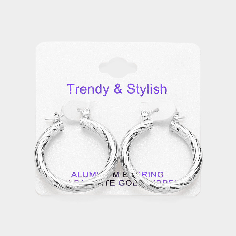 Silver textured hoop earrings with a polished twisted design and pin catch closure, displayed on a white jewelry card against a light background.