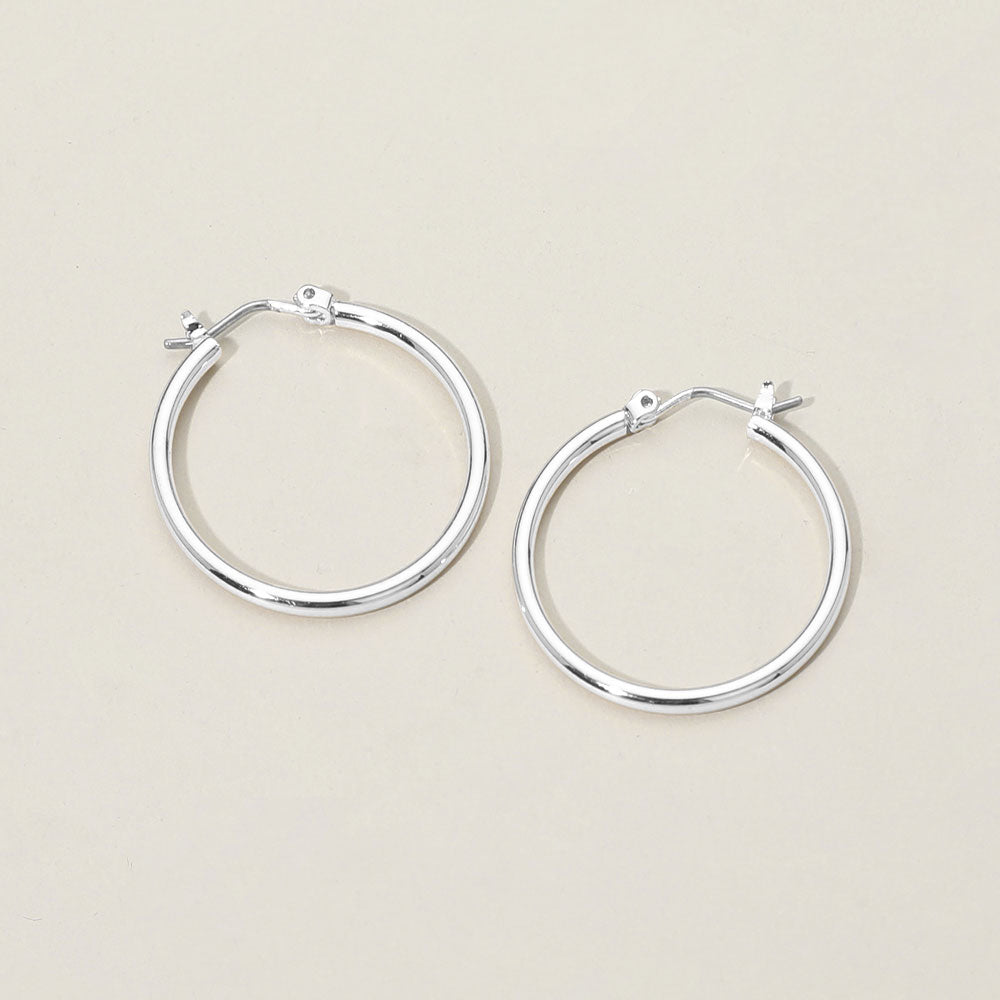A pair of polished pin catch silver hoop earrings on a light beige background.