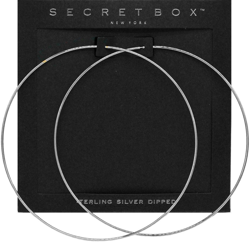 Oversized silver wire hoop earrings with a 4-inch diameter and slide in closure, displayed on a black earring card.
