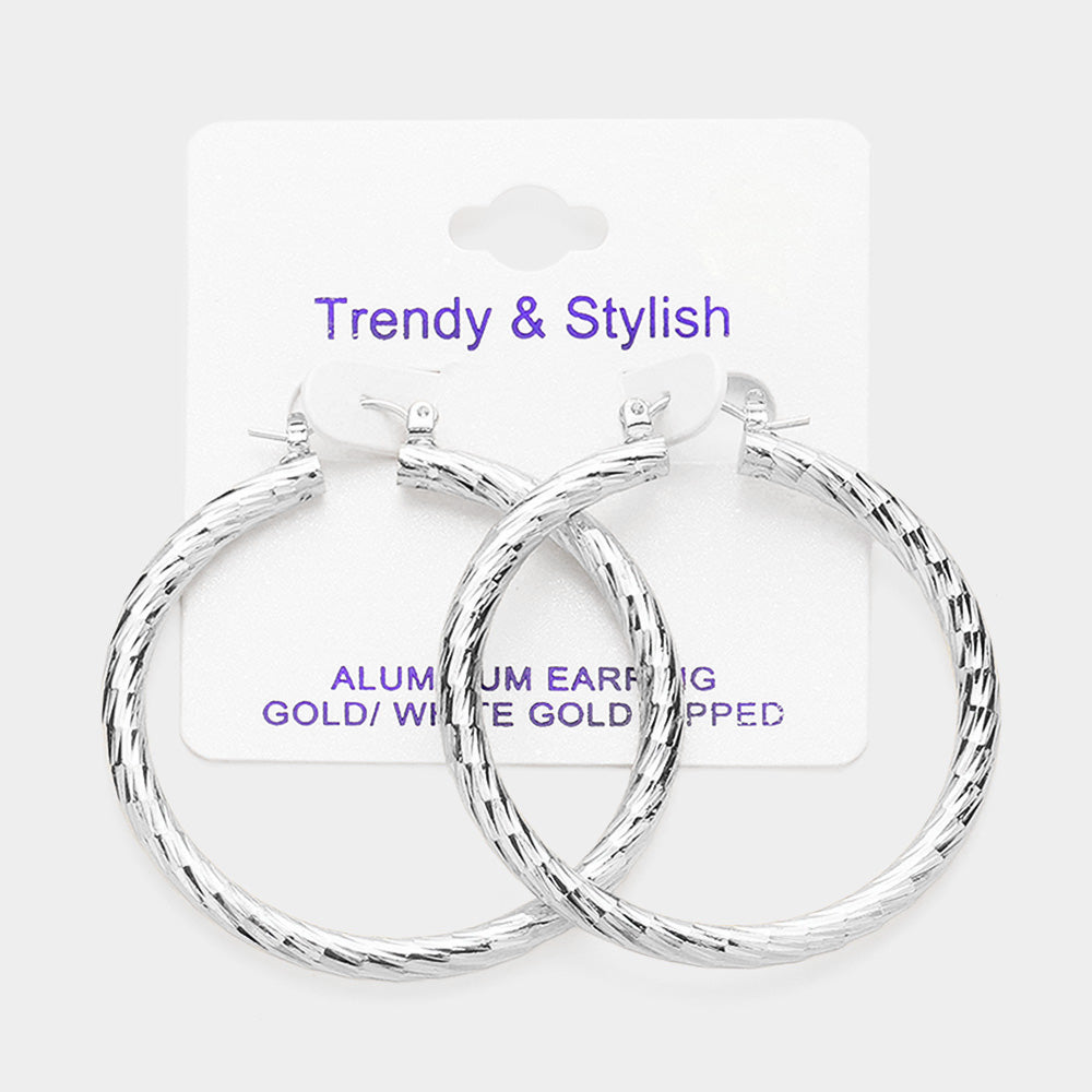 Silver-tone textured hoop earrings with a twisted design and pin catch closure, displayed on a white jewelry card against a light background.