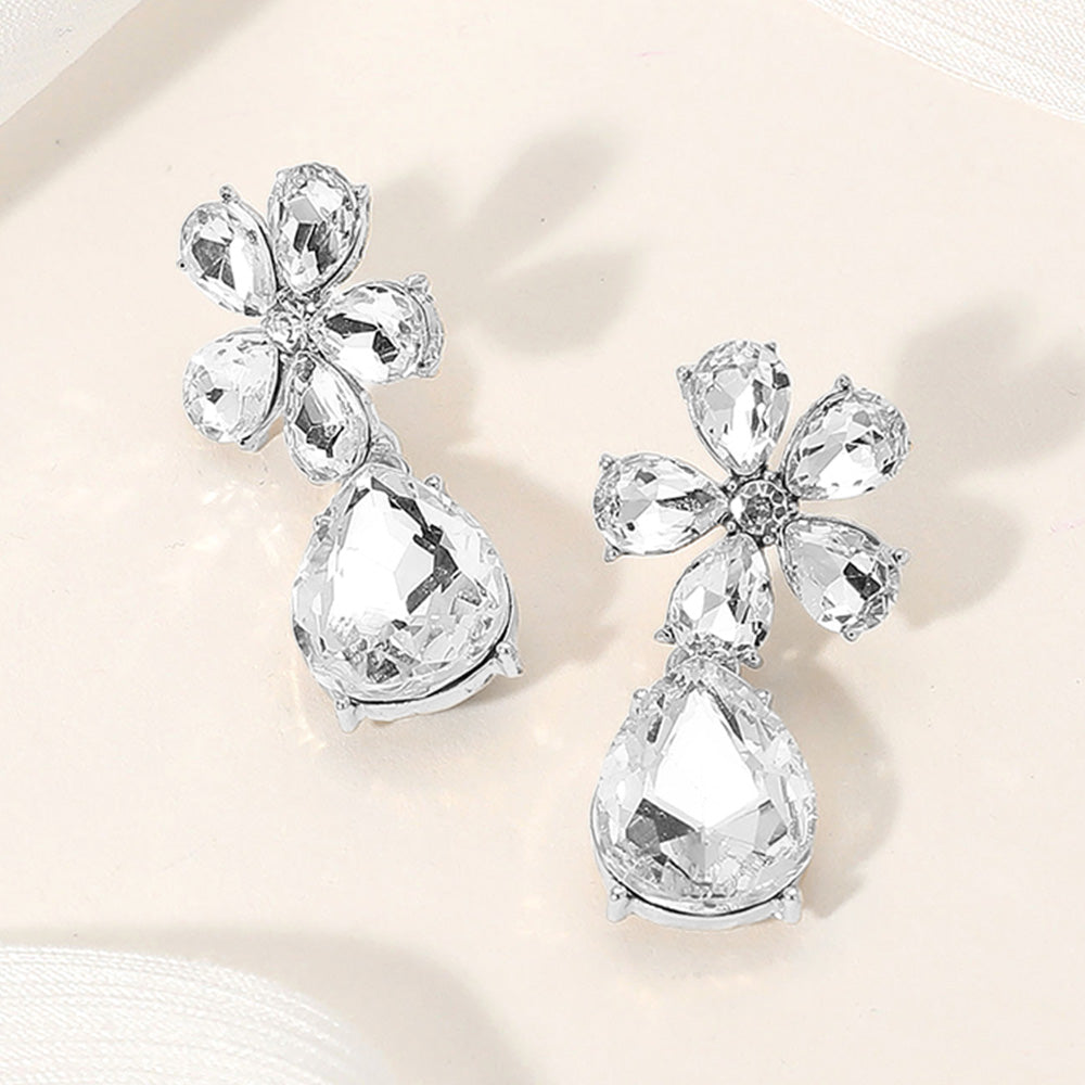 Clear flower and teardrop stone dangle earrings with silver setting for pageant, prom, or wedding wear on a cream color background