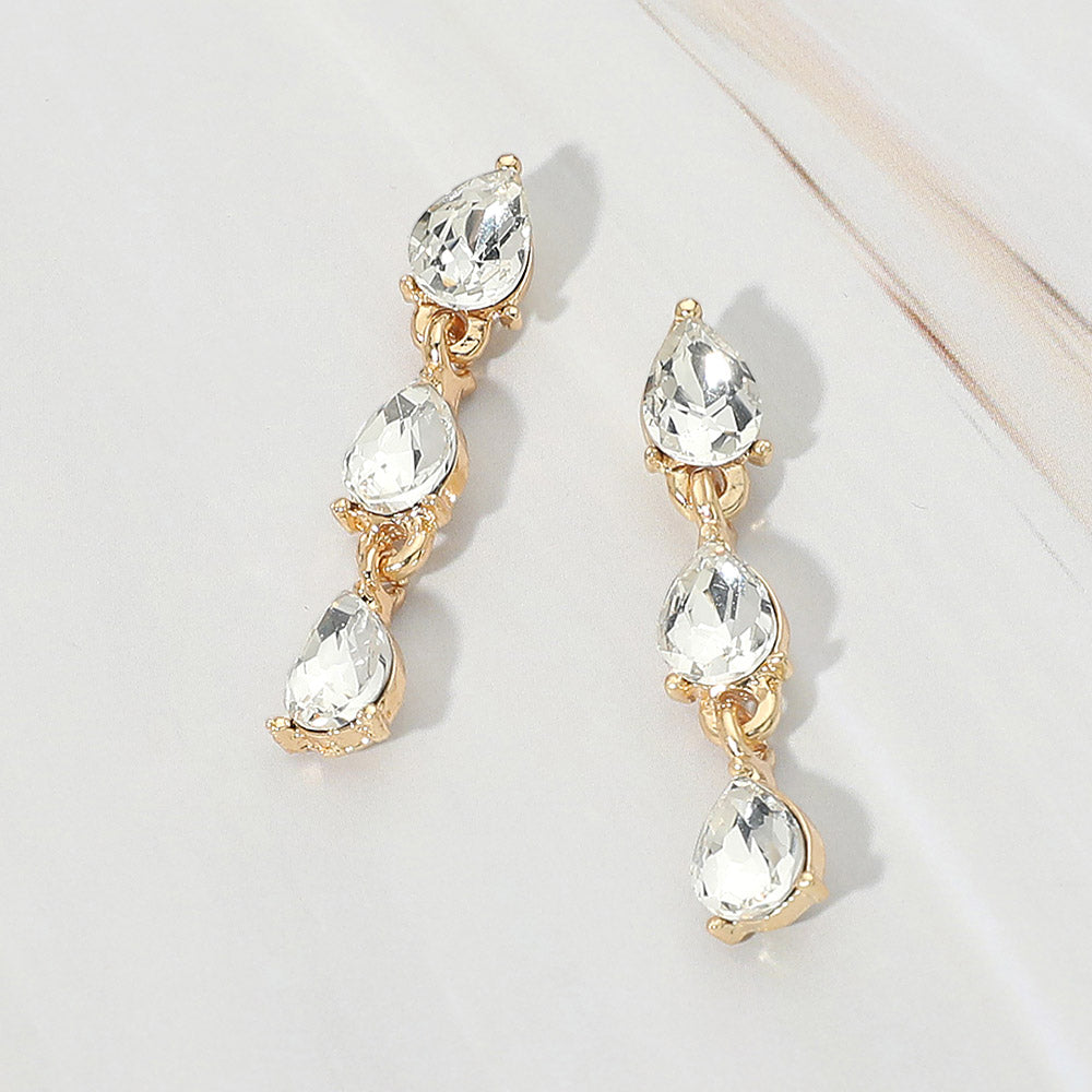 Small clear triple teardrop cluster drop earrings on gold on a white marble background