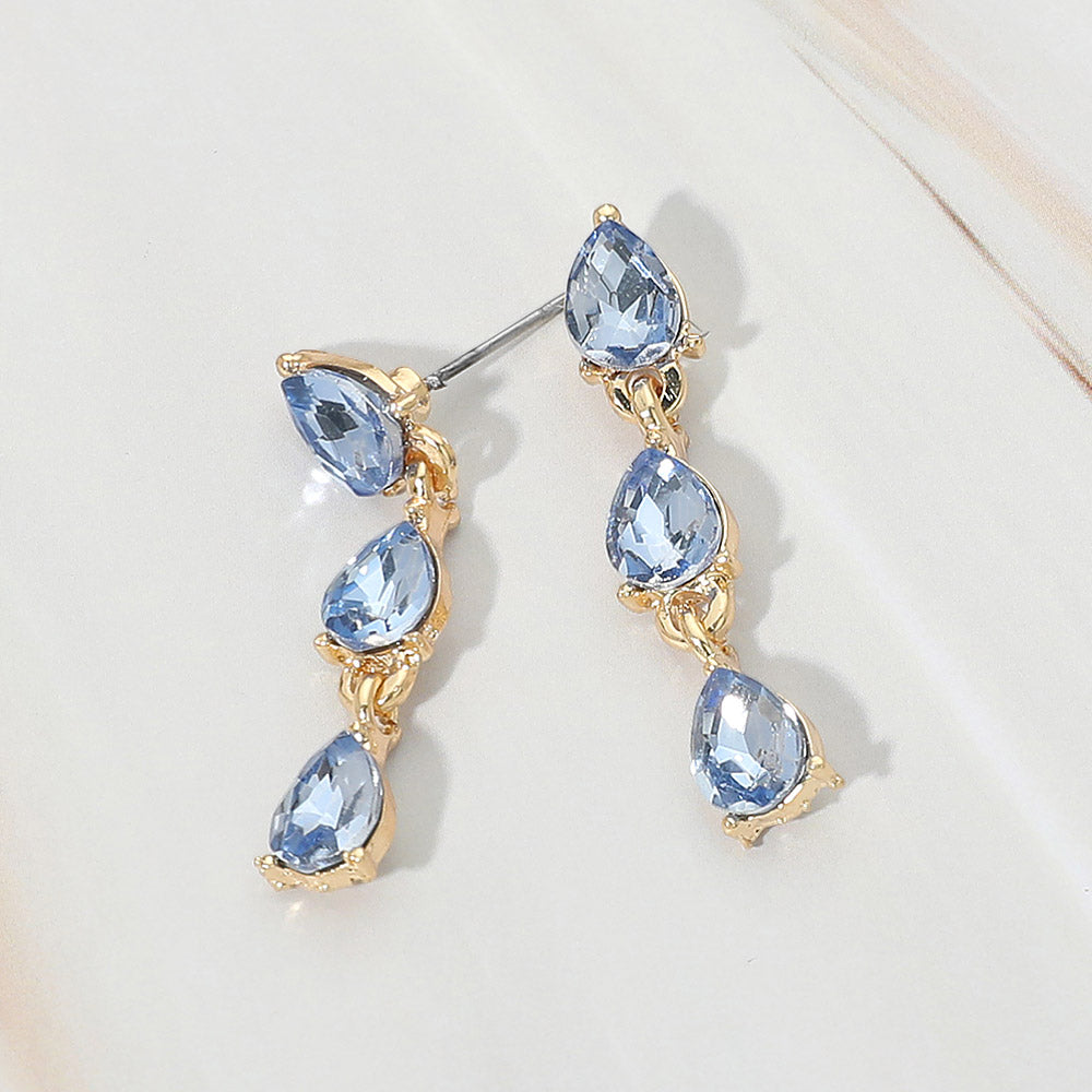 Small light blue triple teardrop cluster drop earrings on gold on a white marble background