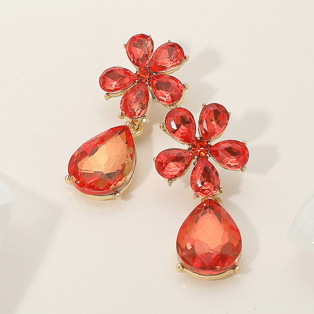 Orange flower and teardrop rhinestone earrings for prom or seasonal pageant fashion on a cream colored background