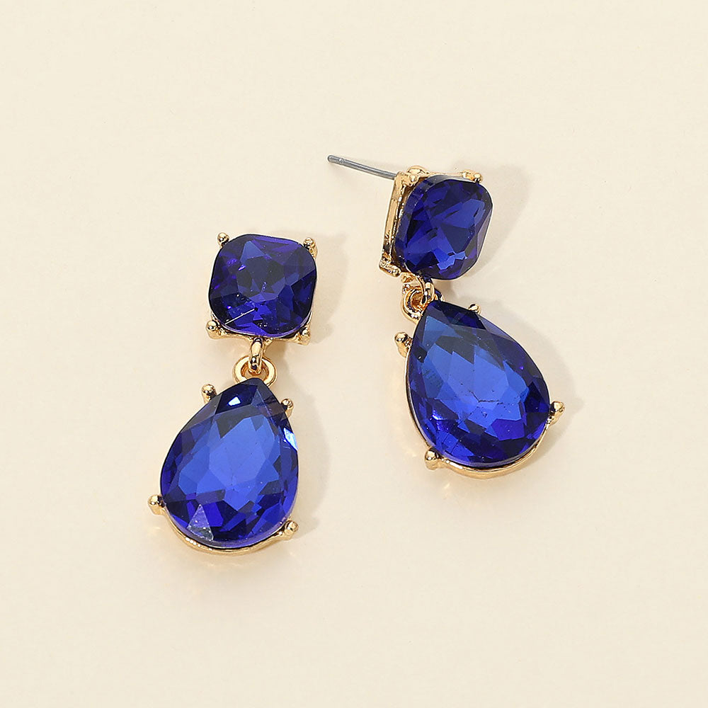 Sapphire Royal Blue crystal drop earrings on gold with a round top stone and large teardrop crystal, displayed on a light cream background.