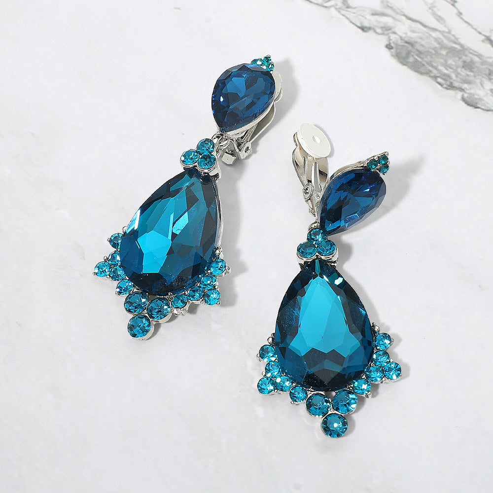Teal faceted teardrop clip-on statement earrings on silver on a white marble background