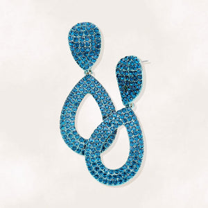 Teal rhinestone pavé cut out teardrop pageant and formal earrings on silver on a beige background