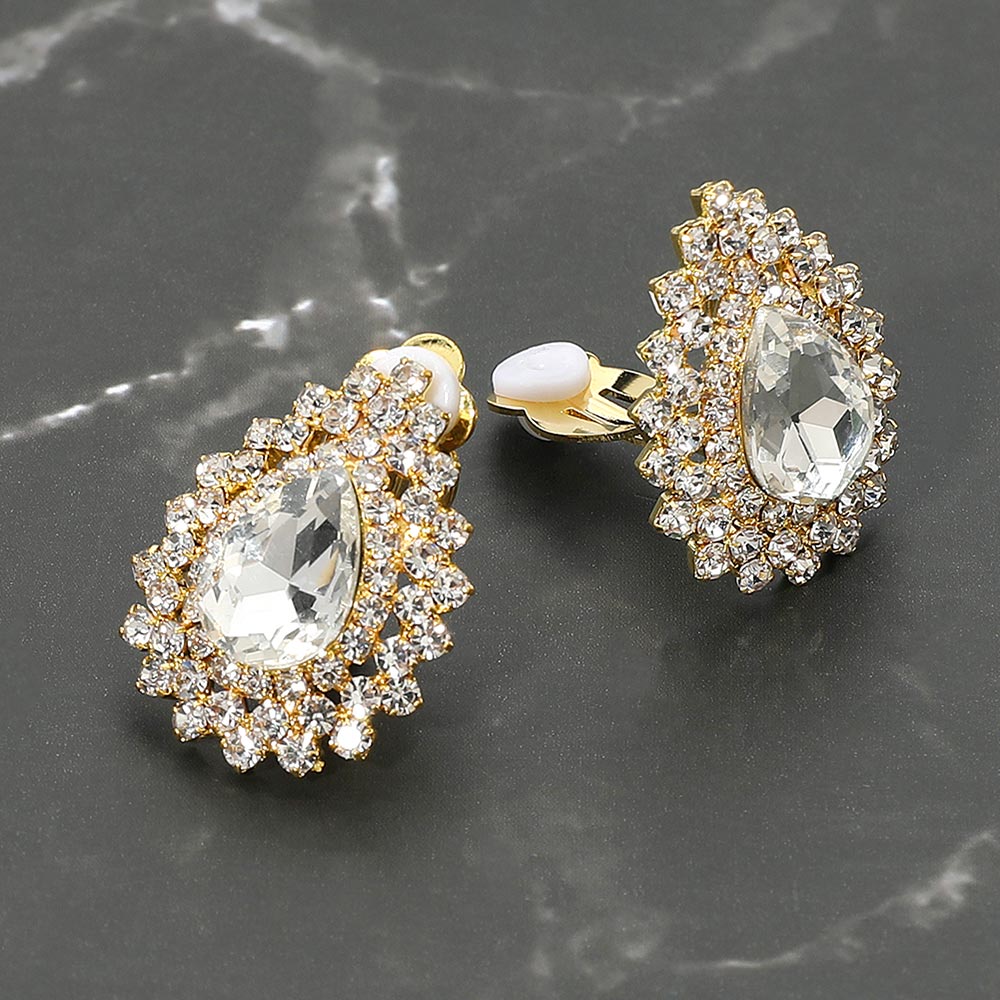 Small clear on gold teardrop crystal cluster clip-on earrings with layered rhinestone halo — elegant non-pierced jewelry for bridal, prom, and evening events on a dark marble background. 