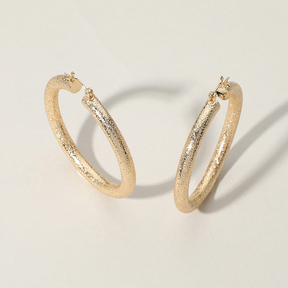 Textured gold metal hoop pin catch earrings on a white background