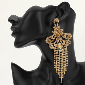 A large ornate Champagne Gold Stone crystal statement earring with cascading bead fringe and clear crystal accents on a black earring mannequin.