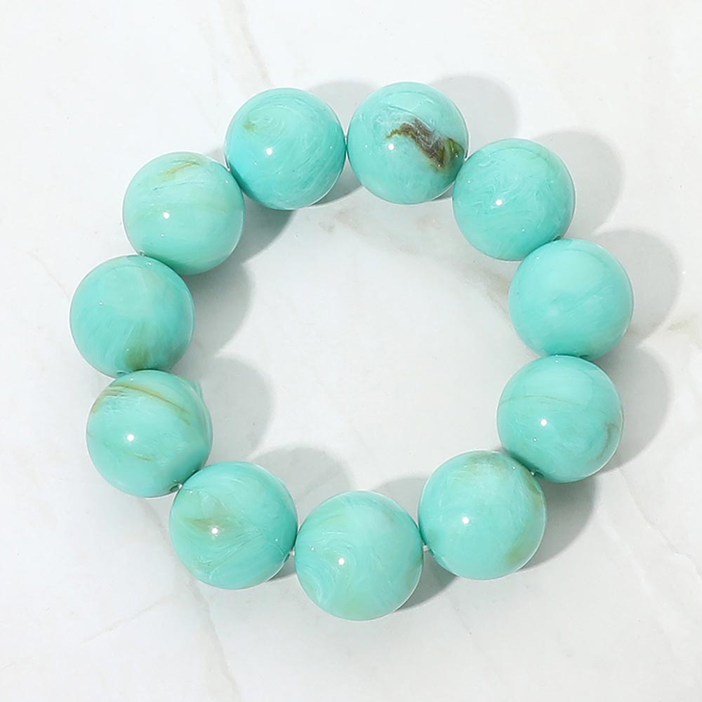 Turquoise chunky ball beaded stretch bracelet with oversized round beads, displayed on a white marble background.