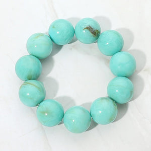 Turquoise chunky ball beaded stretch bracelet with oversized round beads, displayed on a white marble background.