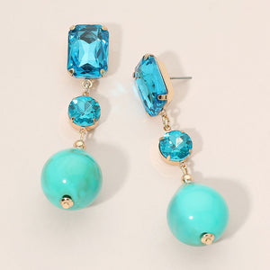Turquoise faceted crystal and ball drop statement earrings on gold with rectangular, round, and spherical turquoise stones, displayed on a light beige background.