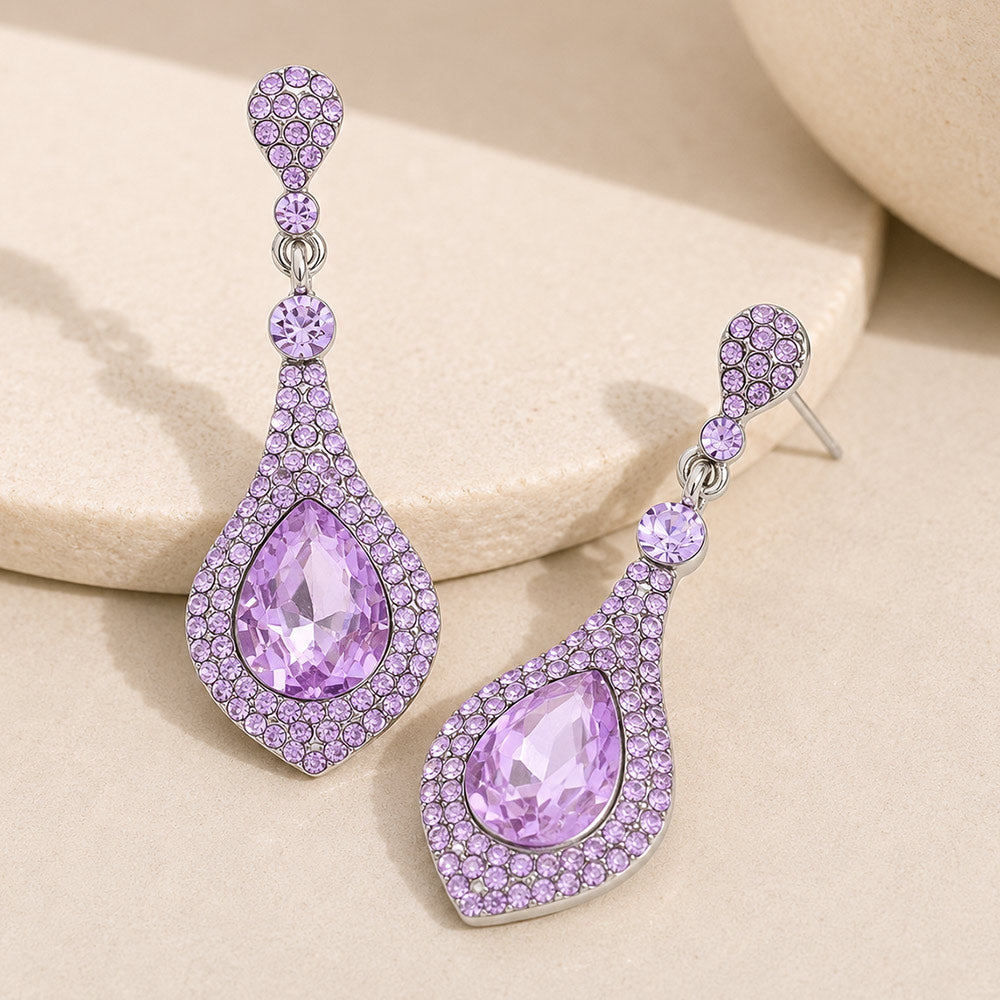 Violet purple crystal teardrop drop earrings on silver featuring a large violet teardrop crystal surrounded by smaller purple crystals, displayed on a neutral beige background.