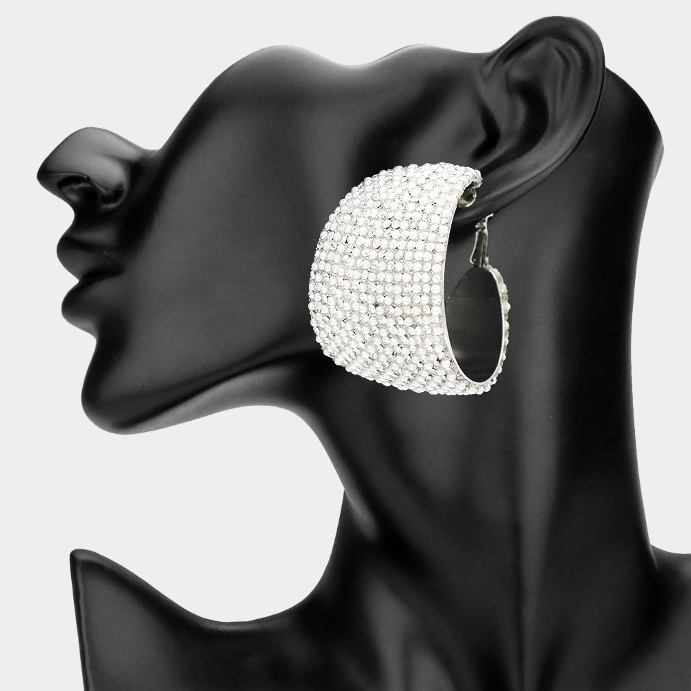 White crystal wide hoop earrings on silver-tone metal with dense faceted rhinestone coverage and omega backs, displayed on a black mannequin profile.