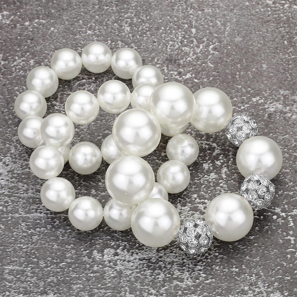 White pearl 3-piece stretch bracelet set with chunky round pearls and crystal-accent spacer details, displayed on a textured gray background.