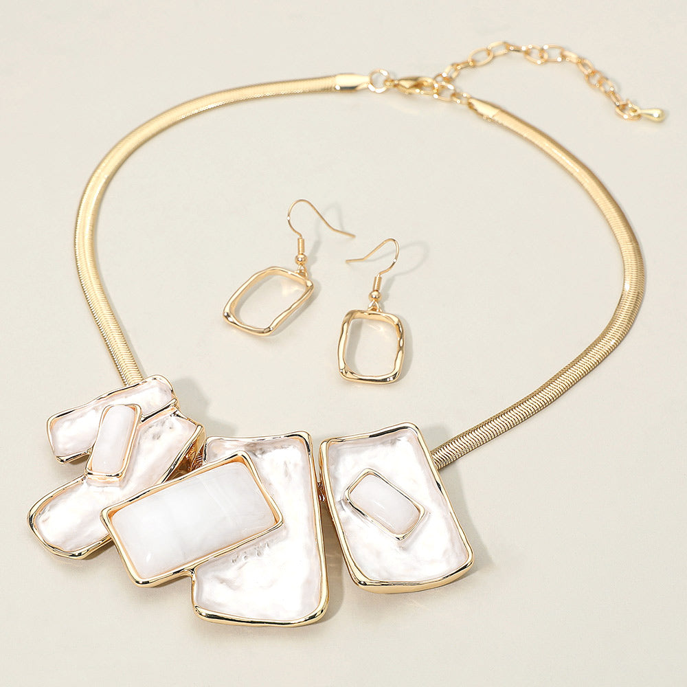 White geometric enamel beaded necklace set with matching earrings – modern statement jewelry for pageant or prom looks. It is on an ivory background.