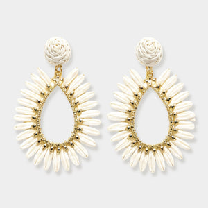 A pair of statement dangle earrings featuring cream-colored textured woven beads in a teardrop shape with a gold-tone metal frame and rose-shaped posts, shown against a light gray background.