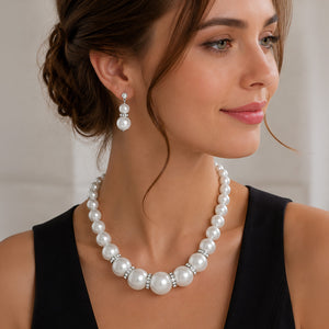 A woman wearing a white oversized pearl and crystal statement necklace with graduated round pearls, crystal accents, and matching drop earrings.
