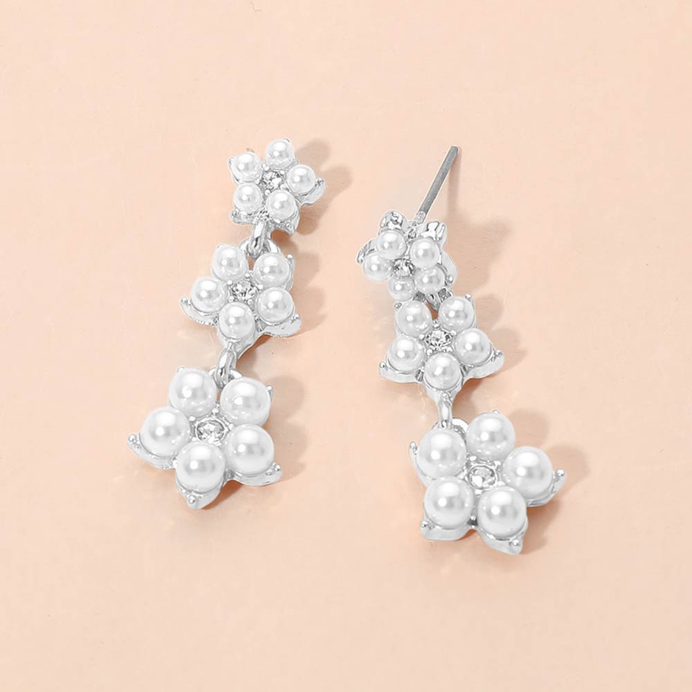 White pearl floral cluster bridal drop earrings in a silver setting on a beige background