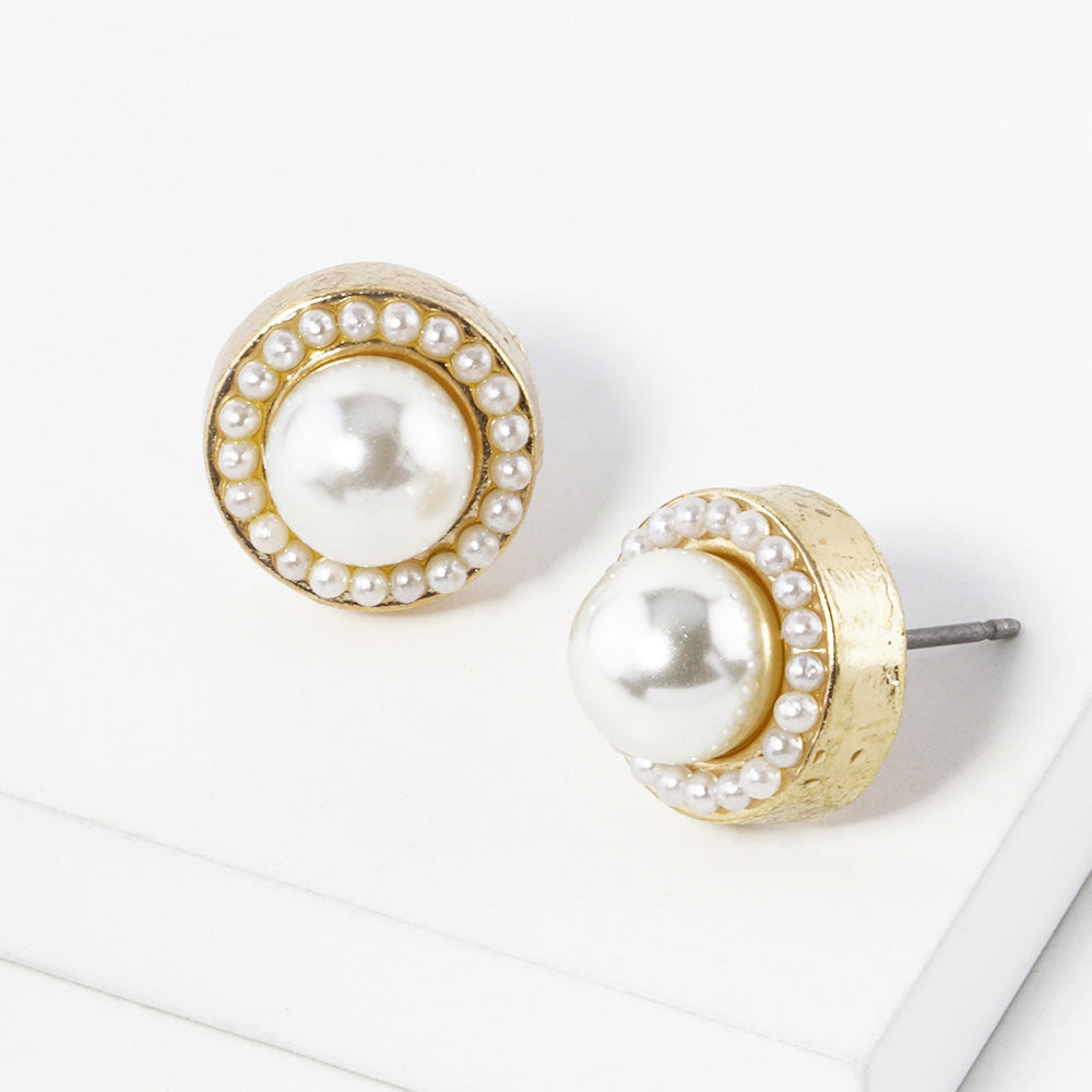 A pair of gold stud earrings with a round white pearl center surrounded by a halo of small clear rhinestones, displayed on a clean white surface.