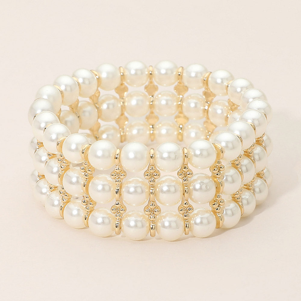 Wide cream pearl bridal stretch bracelet with gold spacer details and layered bead design on a light beige background