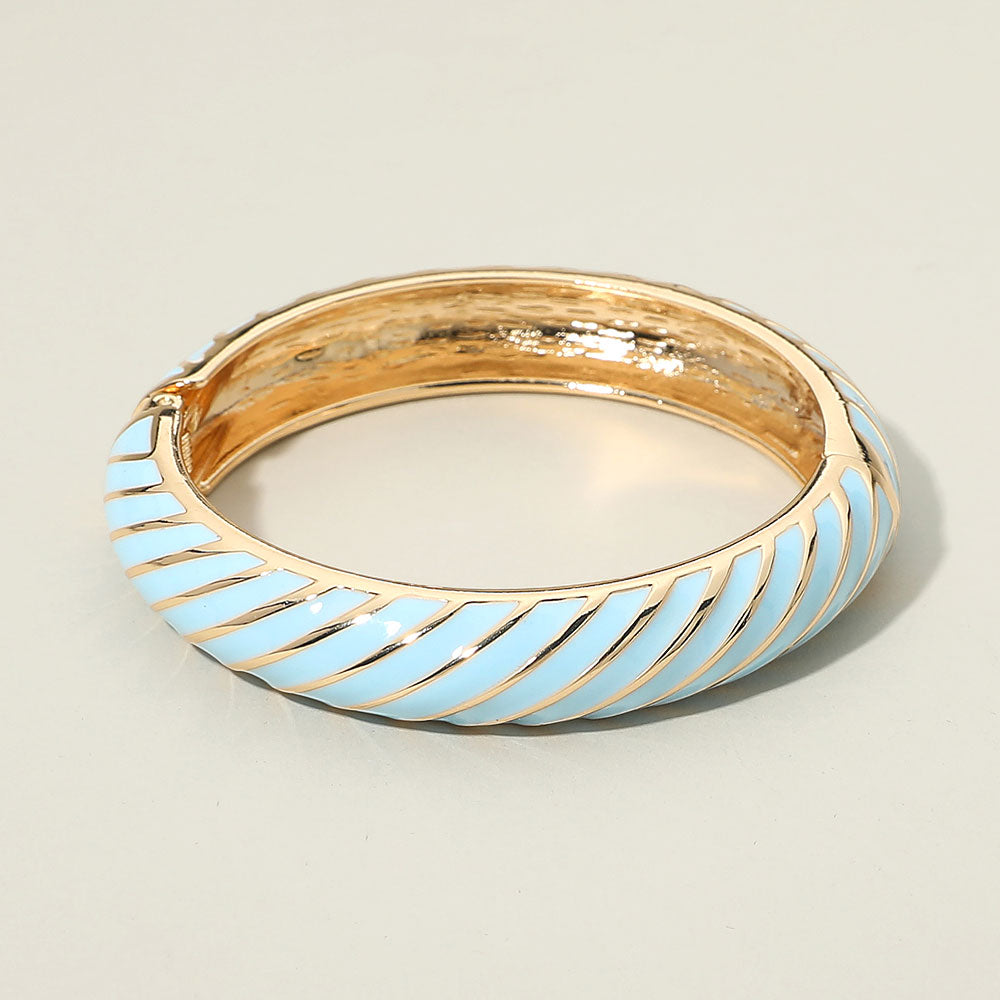 Wide light blue twisted hinged bangle bracelet on gold on a light beige background
