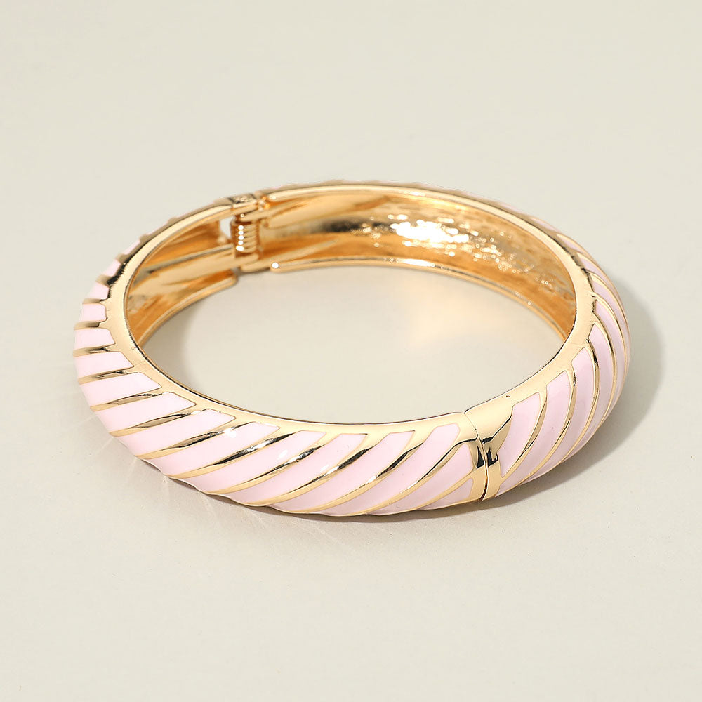 Wide light pink twisted hinged bangle bracelet on gold on a light beige background