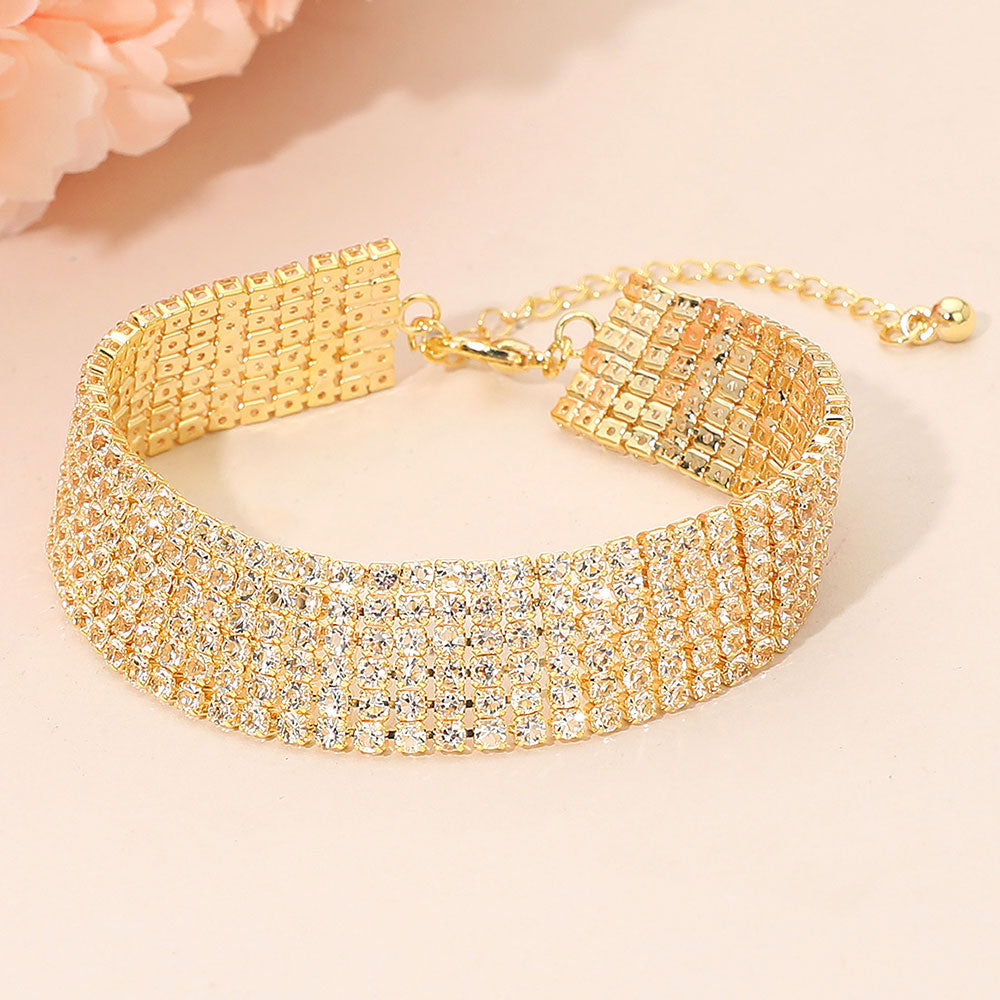 Wide multi-row clear crystal rhinestone bracelet on gold displayed on a beige background.