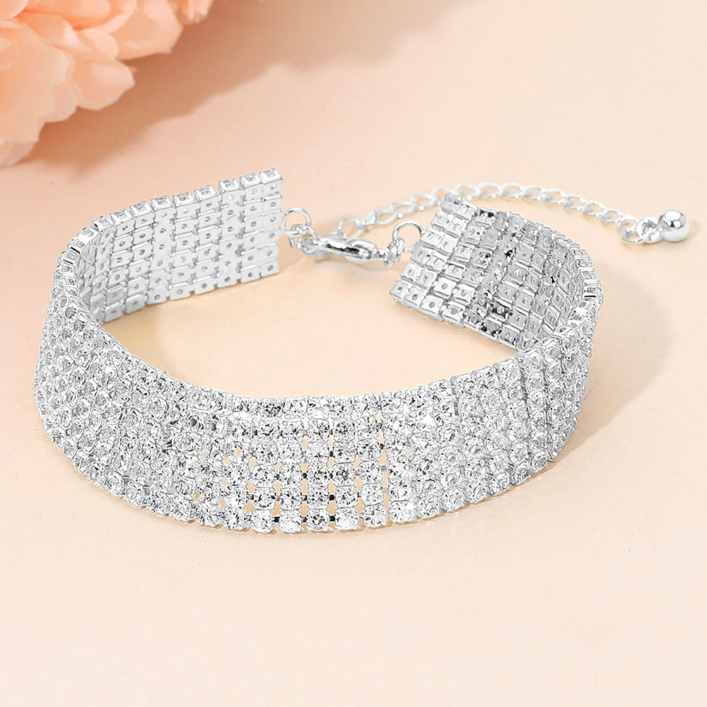 Wide multi-row clear crystal rhinestone bracelet on silver displayed on a beige background.