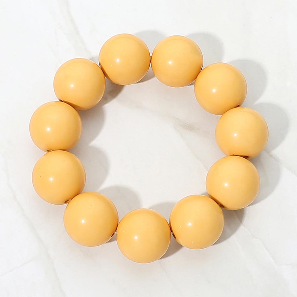 Yellow chunky ball beaded stretch bracelet with oversized round beads, displayed on a white marble background.