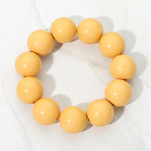 Yellow chunky ball beaded stretch bracelet with oversized round beads, displayed on a white marble background.