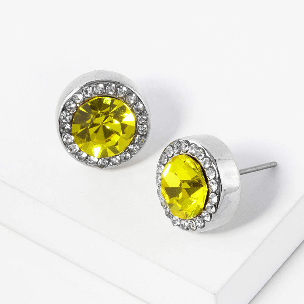 A pair of silver stud earrings with an oval yellow faceted center stone surrounded by a halo of small clear rhinestones, displayed on a clean white surface.