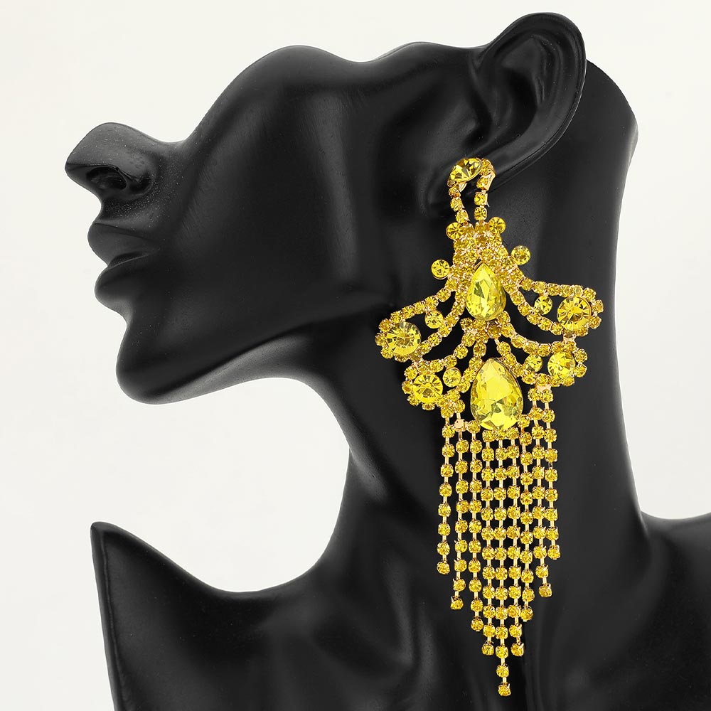 A woman wearing a large ornate yellow crystal statement earring with cascading bead fringe and yellow crystal accents against a light gray background.